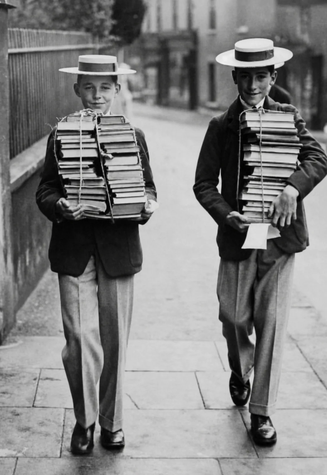 Two schoolboys in boater hats carrying stacks of books, entrance to the EDMONT Library