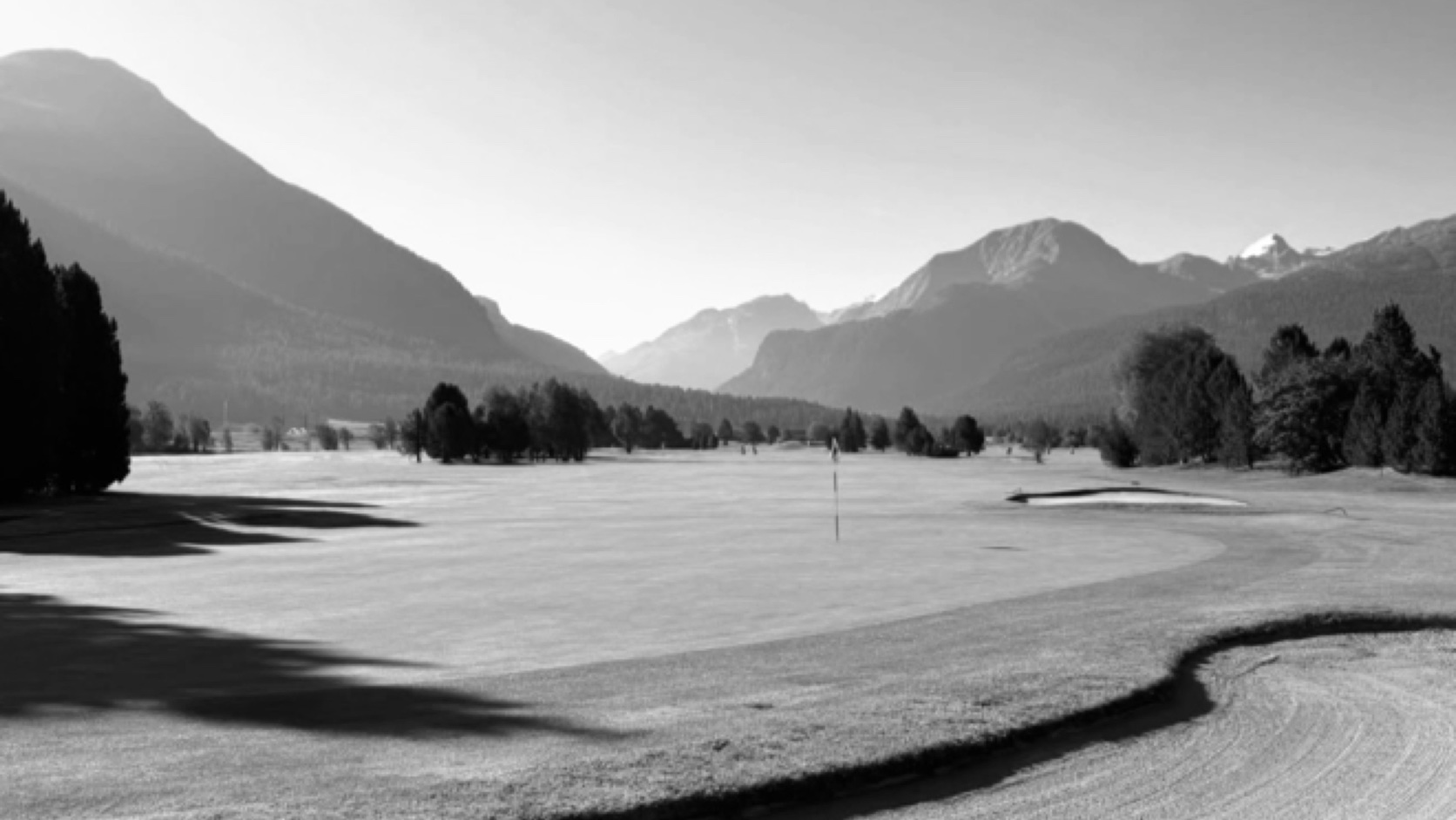An Alpine valley with mountains on the horizon, in black and white