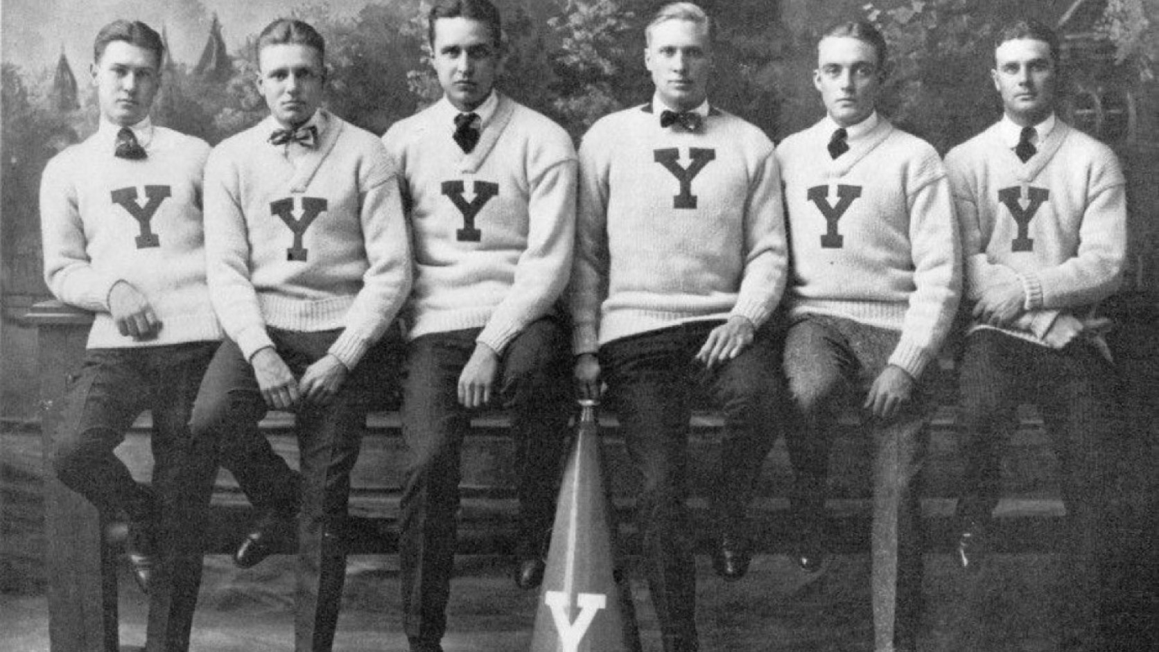 A historic photograph of six Yale students in letter sweaters beside a megaphone bearing the same Y