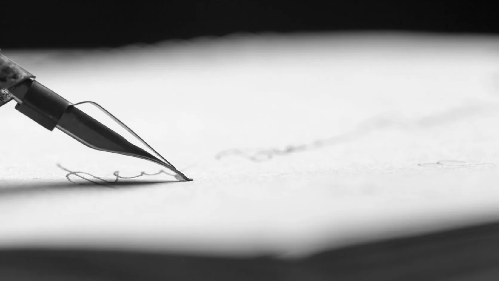 A close-up of a dip pen writing lines of a letter on paper