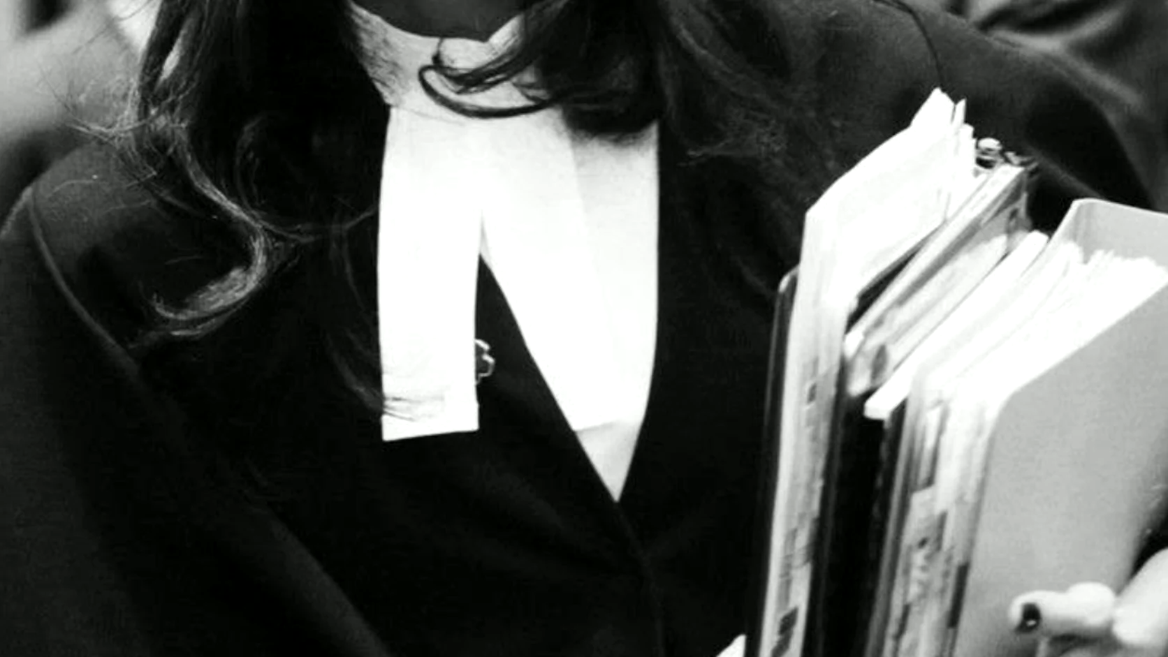 A student in academic dress carrying a stack of folders and papers