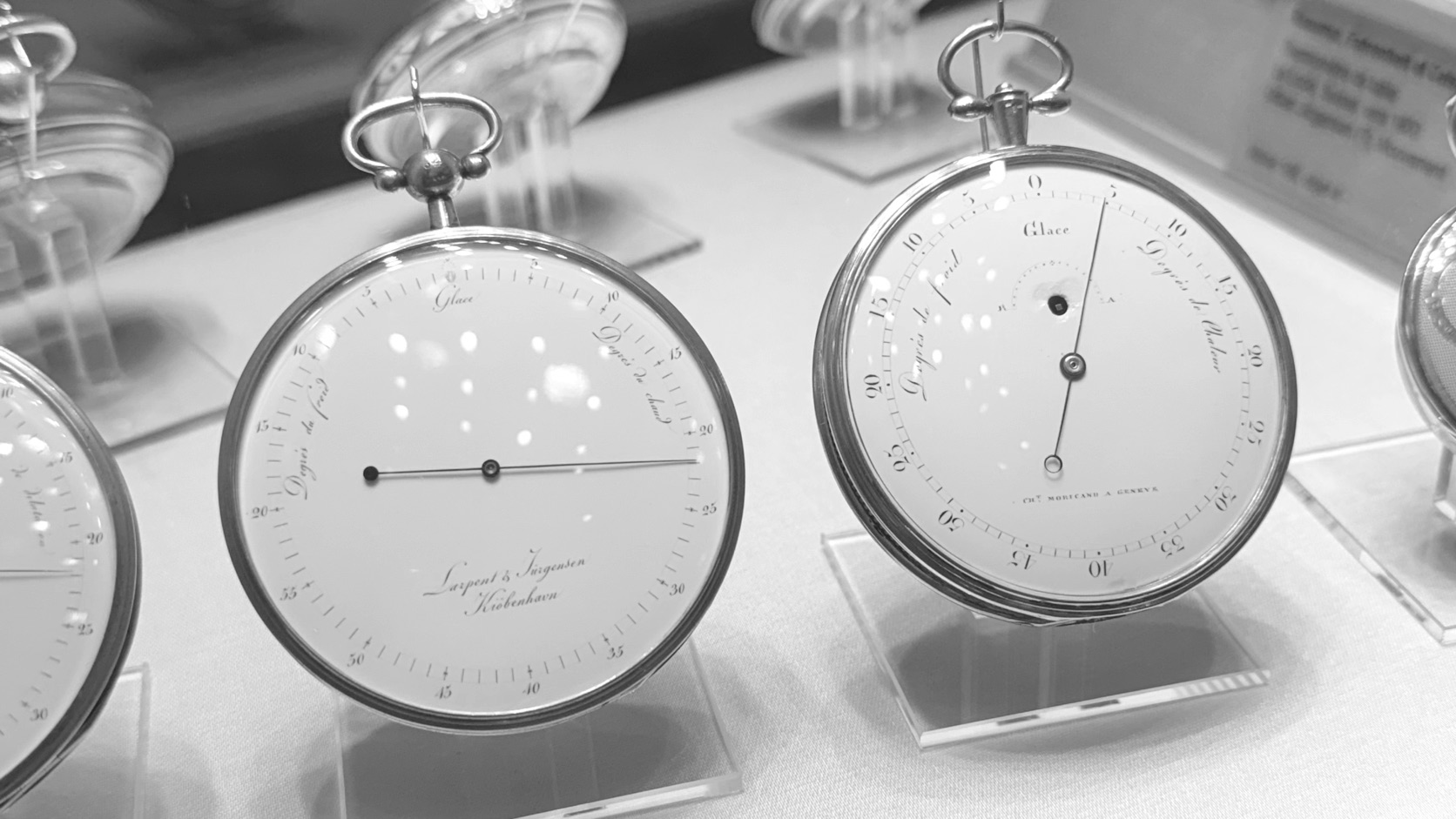 Two antique pocket instruments with graduated dials in a museum case, black and white